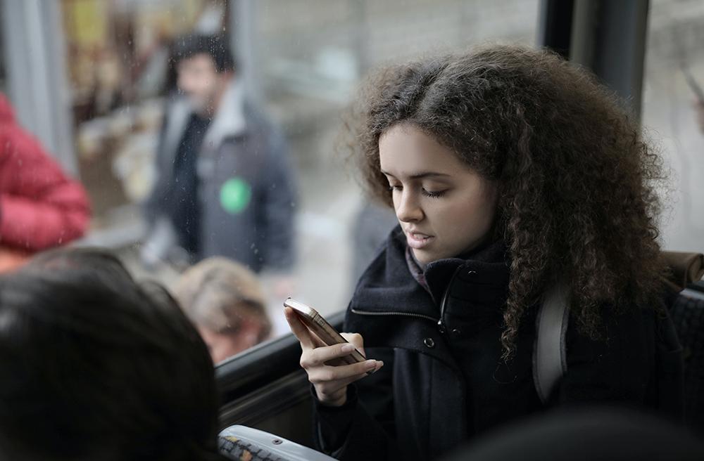 Chica sentada en el bus, al lado de la ventana, consultando el móvil